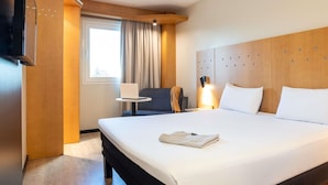 Una habitación de hotel con una cama grande, un escritorio con una computadora portátil, una silla y un televisor montado en la pared.