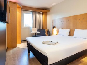 Una habitación de hotel con una cama grande, un escritorio con una computadora portátil, una silla y un televisor montado en la pared.