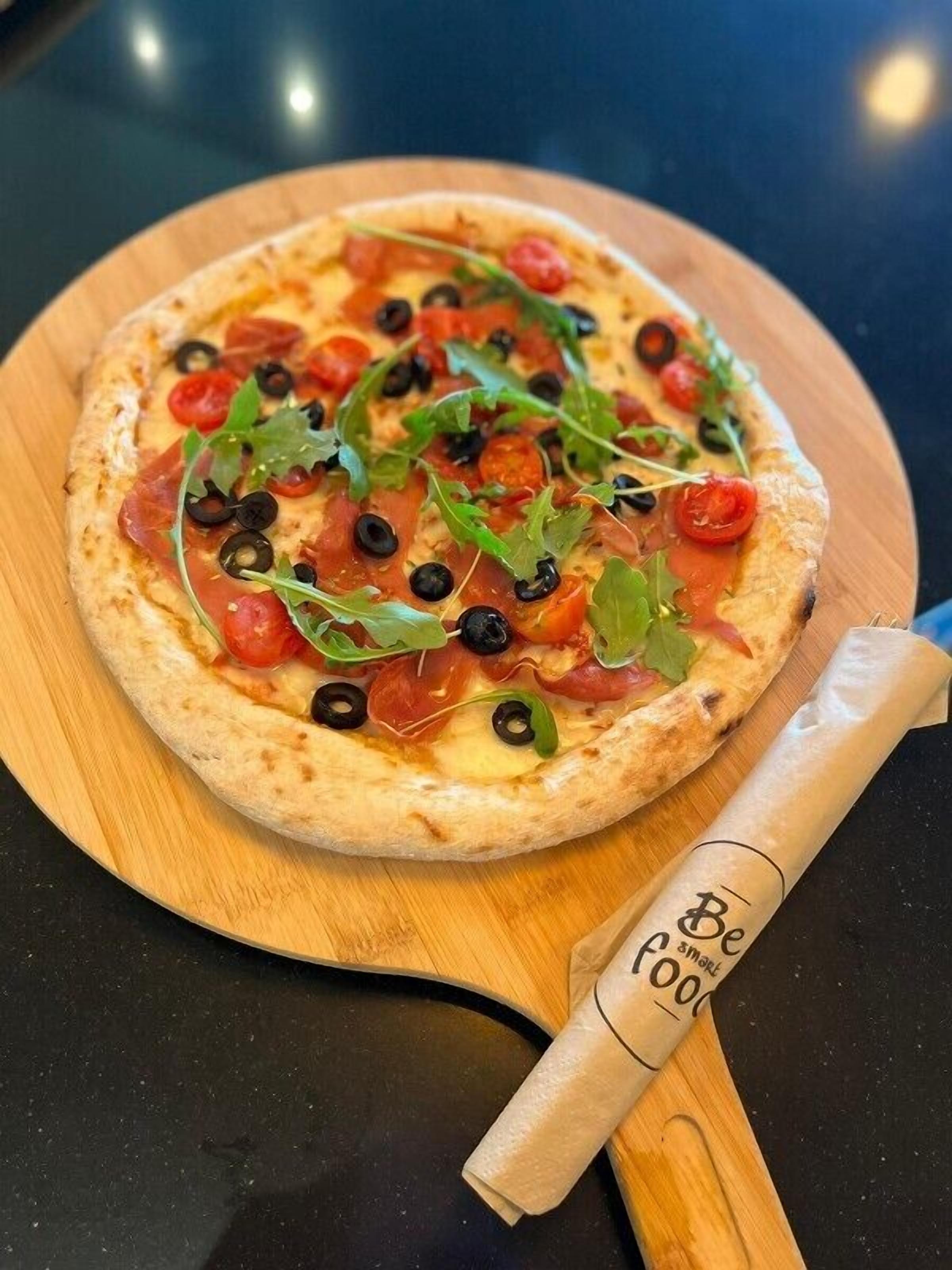 Una pizza sobre una tabla de madera, junto a un cortador de pizza.