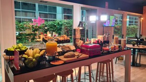Una barra de desayuno con distintos alimentos, una máquina de café y vistas al jardín exterior.