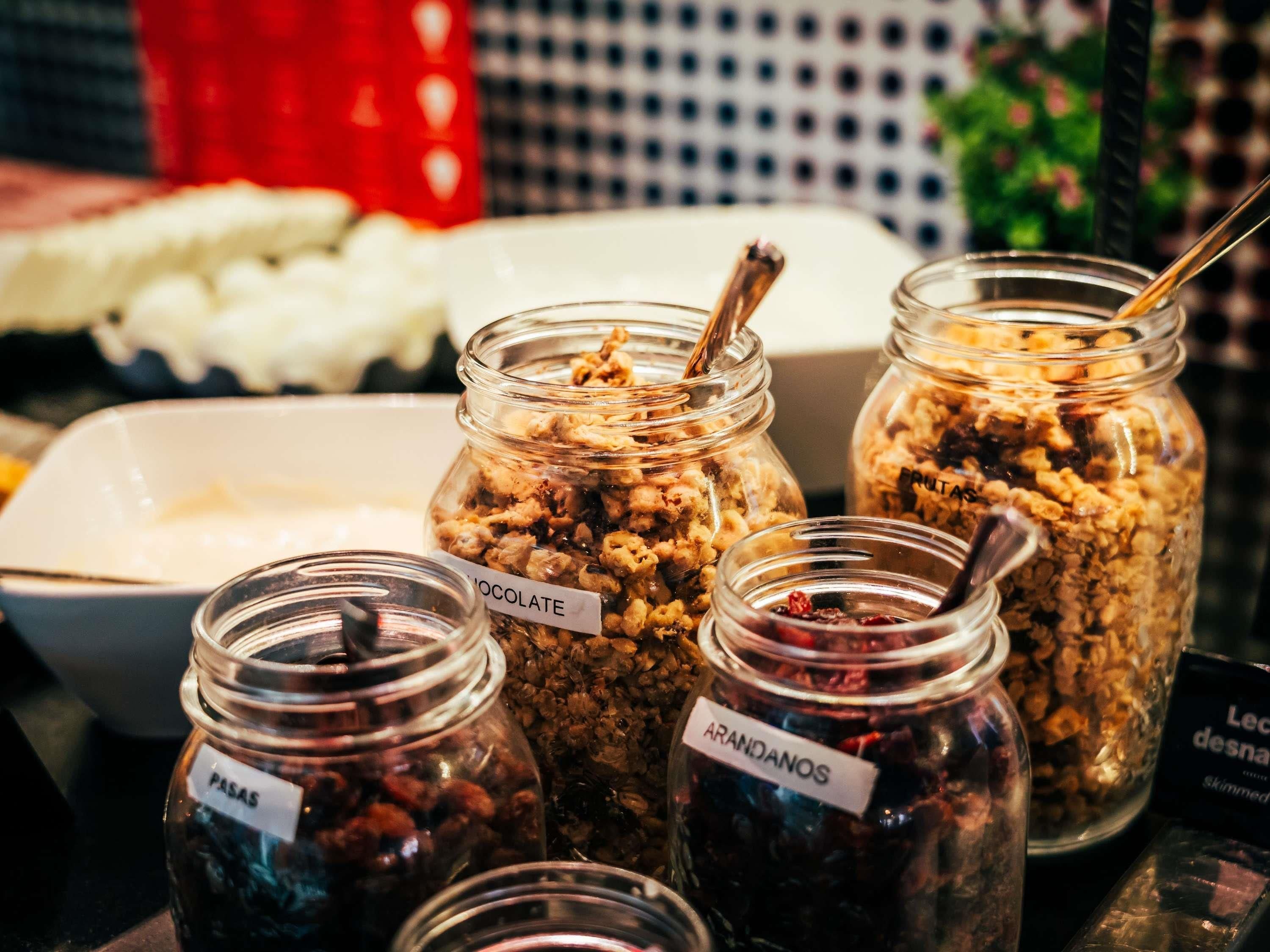Variedad de alimentos en frascos de vidrio con etiquetas que indican sabores como chocolate, fruta y pasas.