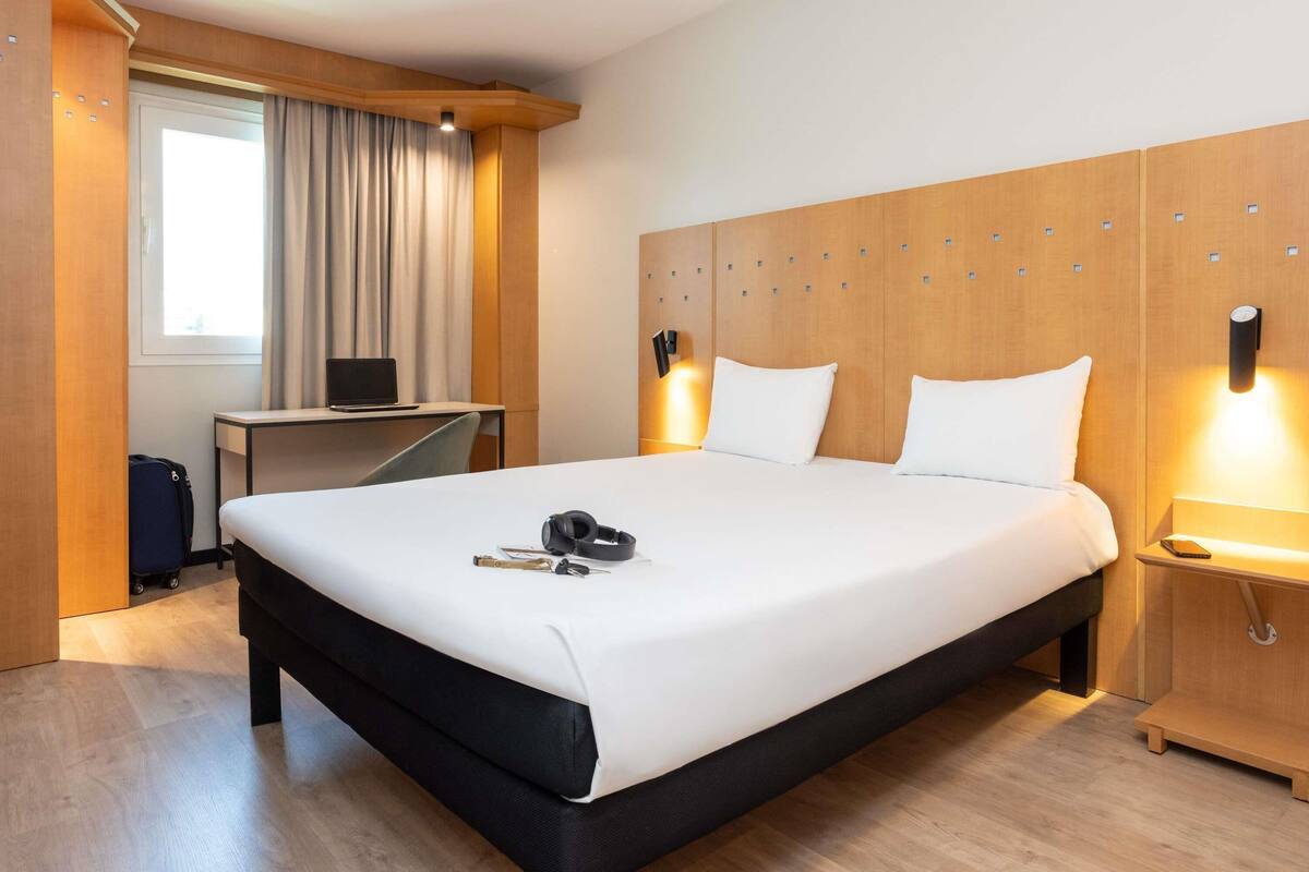 Una habitación de hotel con una cama grande, un escritorio, una computadora portátil y una maleta.