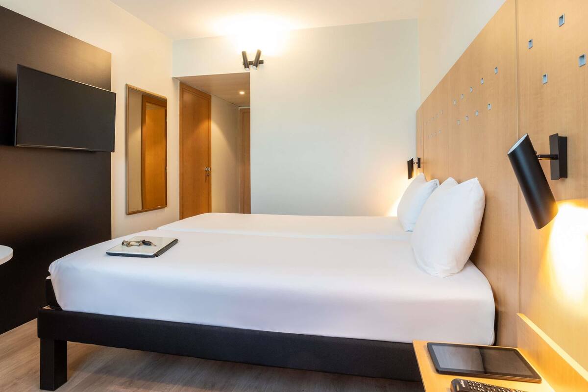 Habitación de hotel moderna con una cama grande, mesitas de noche, un televisor de pantalla plana y una pared decorativa de madera.