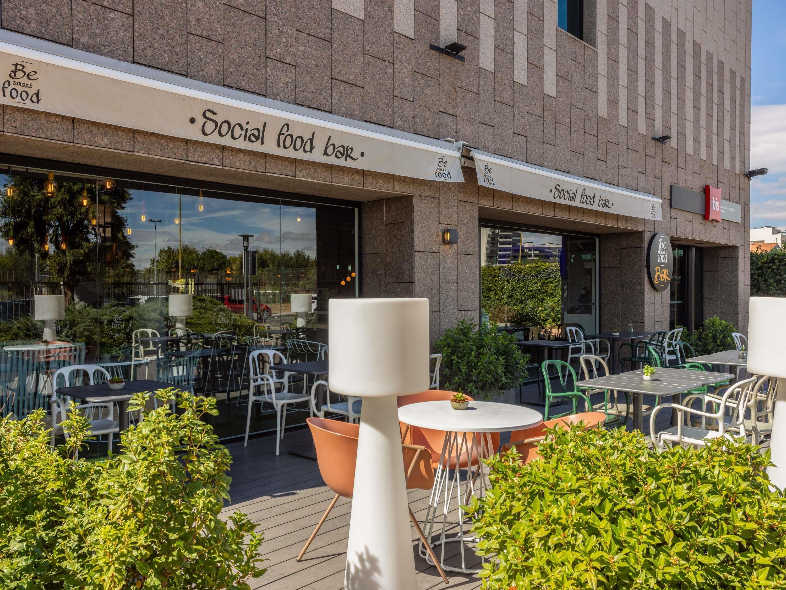 An outdoor seating area with tables and chairs, a sign reading 'Social food bar,' and a building facade with a stone texture.