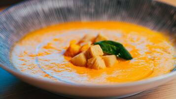 Un tazón de sopa de color naranja cremoso, adornada con una hoja verde y cubos de comida encima.