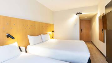 Een hotelkamer met twee bedden, een houten hoofdeinde, nachtlampjes en een deur naar een andere kamer.