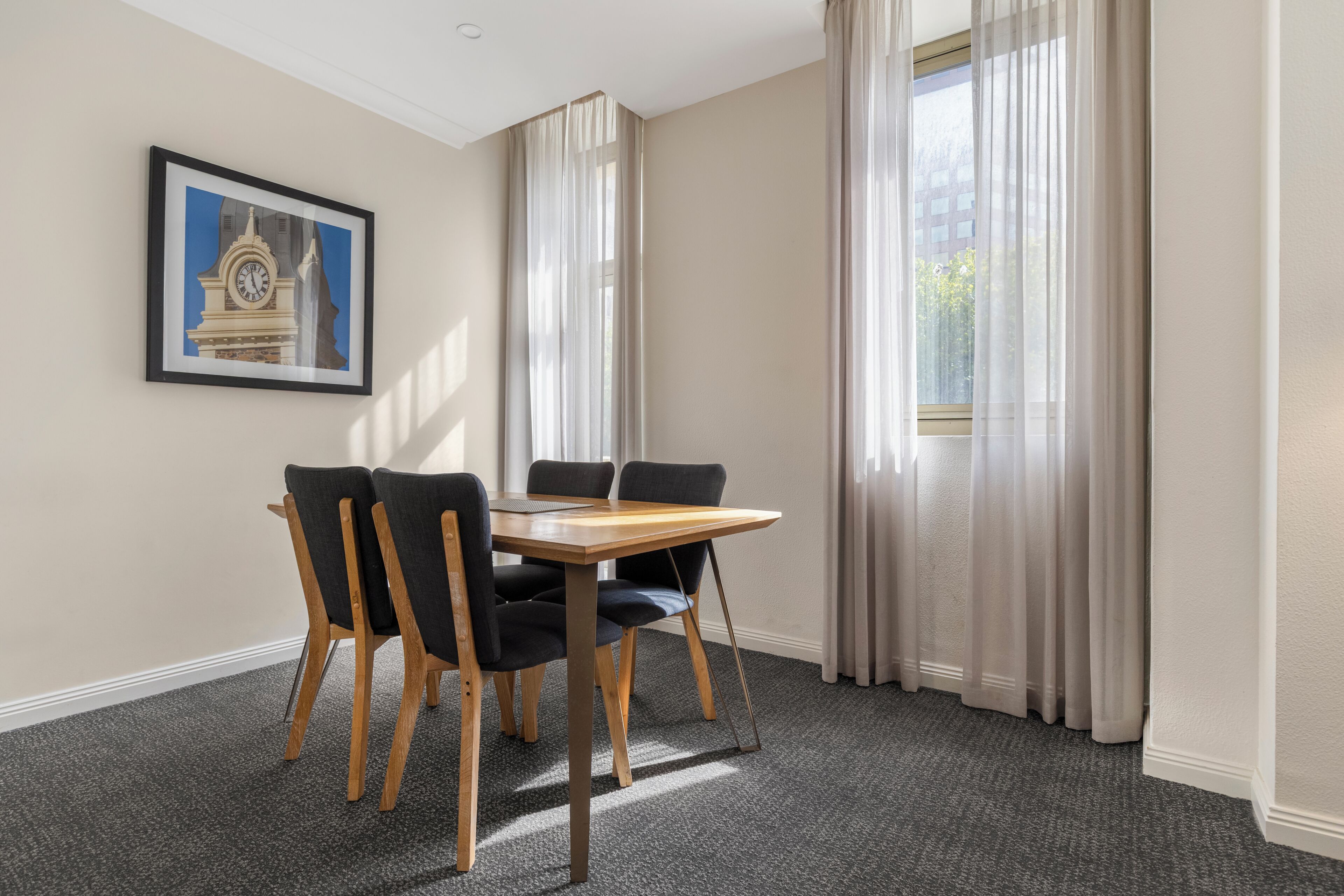 A room with a table and chairs, a framed picture on the wall, and curtains on the windows.