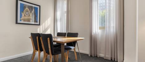 A room with a table and chairs, a framed picture on the wall, and curtains on the windows.
