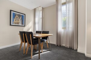 Une pièce avec une table et des chaises, un tableau encadré au mur et des rideaux aux fenêtres.