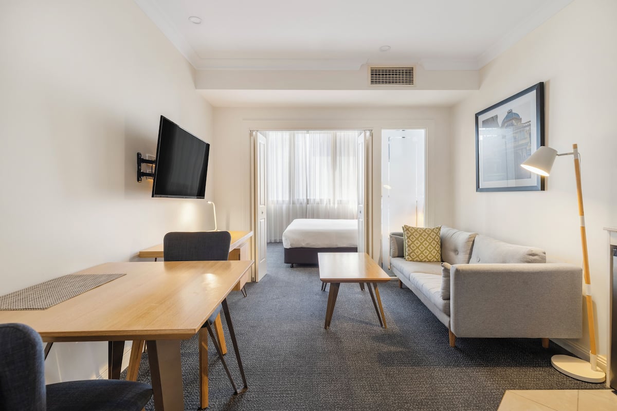 Een hotelkamer met een bed, een slaapbank, een bureau, een televisie en een ingelijste foto aan de muur.