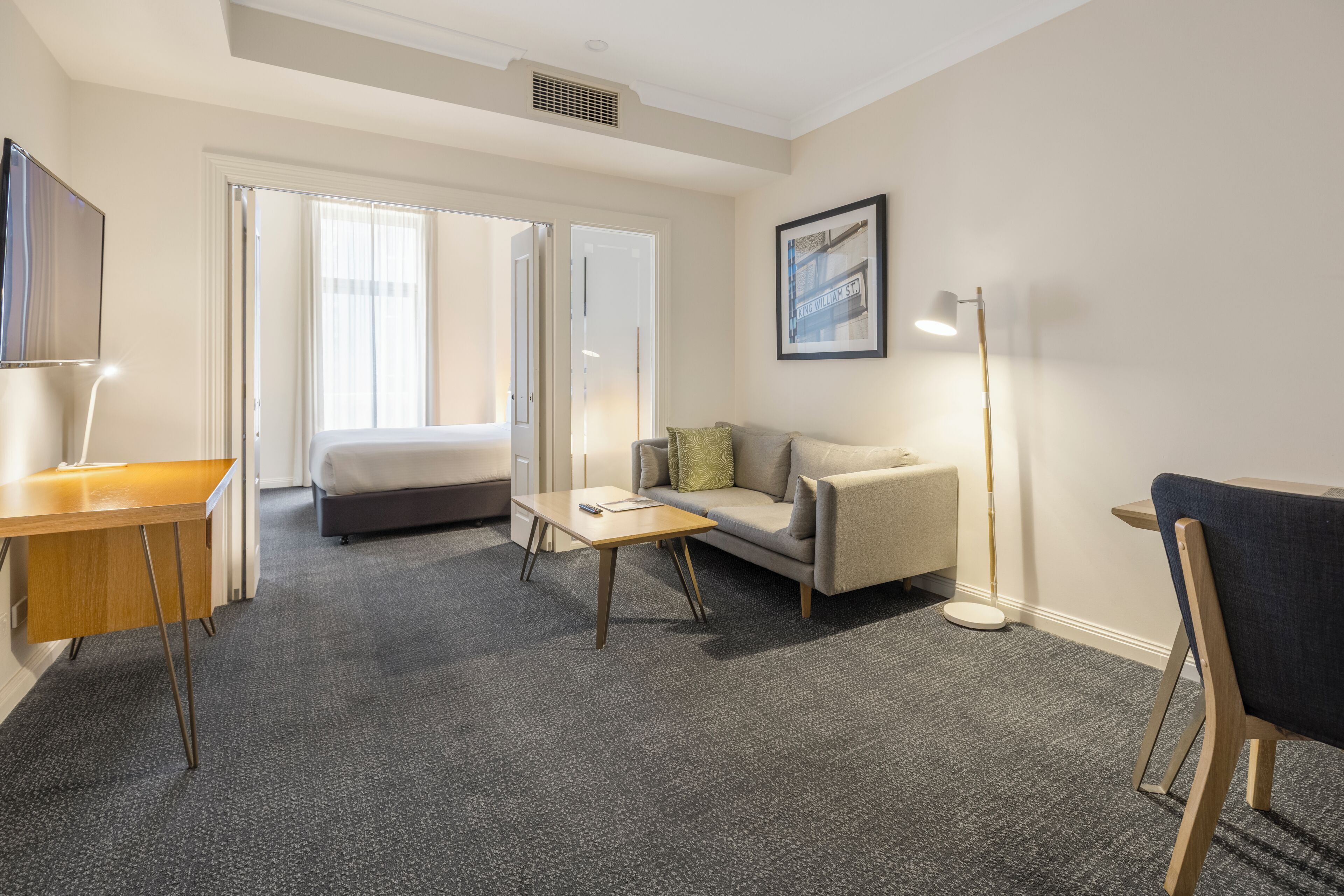 Een hotelkamer met een bed, een bank, een bureau, een lamp en een lijst met foto aan de muur.