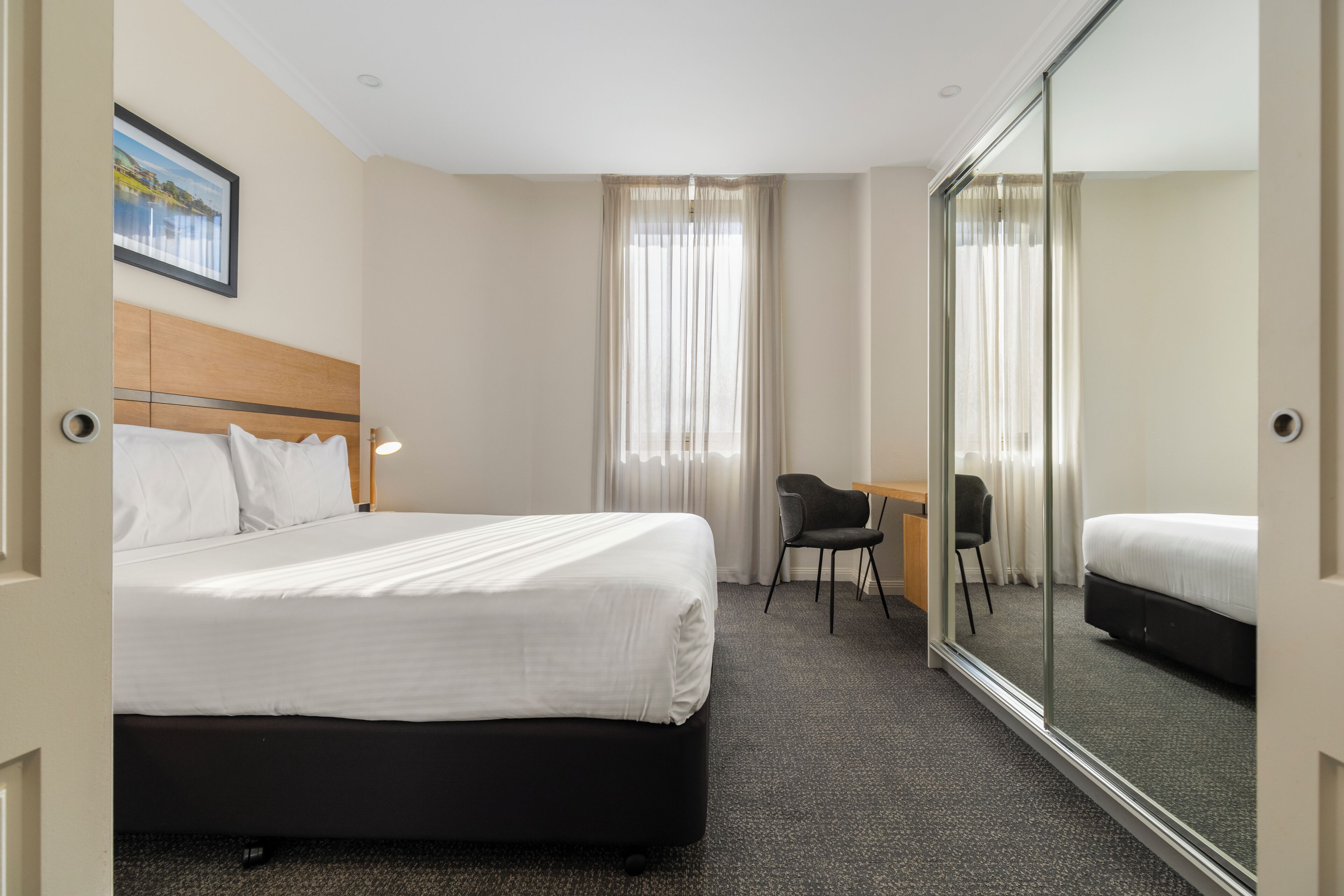 Una habitación de hotel con una cama, un escritorio, una silla y un espejo grande.
