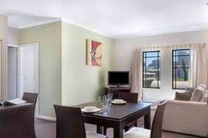 A hotel room with a dining area, a TV, and a view of the city. - Frome Apartments (Adelaide)