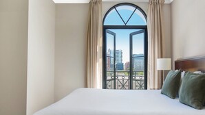 Una habitación de hotel con una cama grande, vistas a través de una ventana con cortinas y una barandilla de balcón.