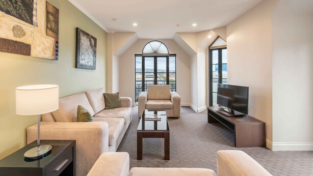 Una sala de estar moderna con sofá, sillón, mesa de centro y televisor. Hay cuadros en la pared y un ventanal con vistas.