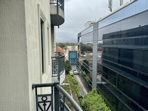 A modern building with a glass facade, a visible balcony, and a street view with parked cars and greenery. - Frome Apartments (Adelaide)