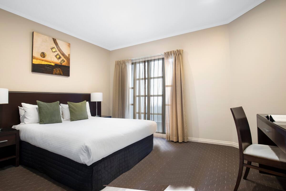 A hotel room with a large bed, a desk, and a window with curtains.