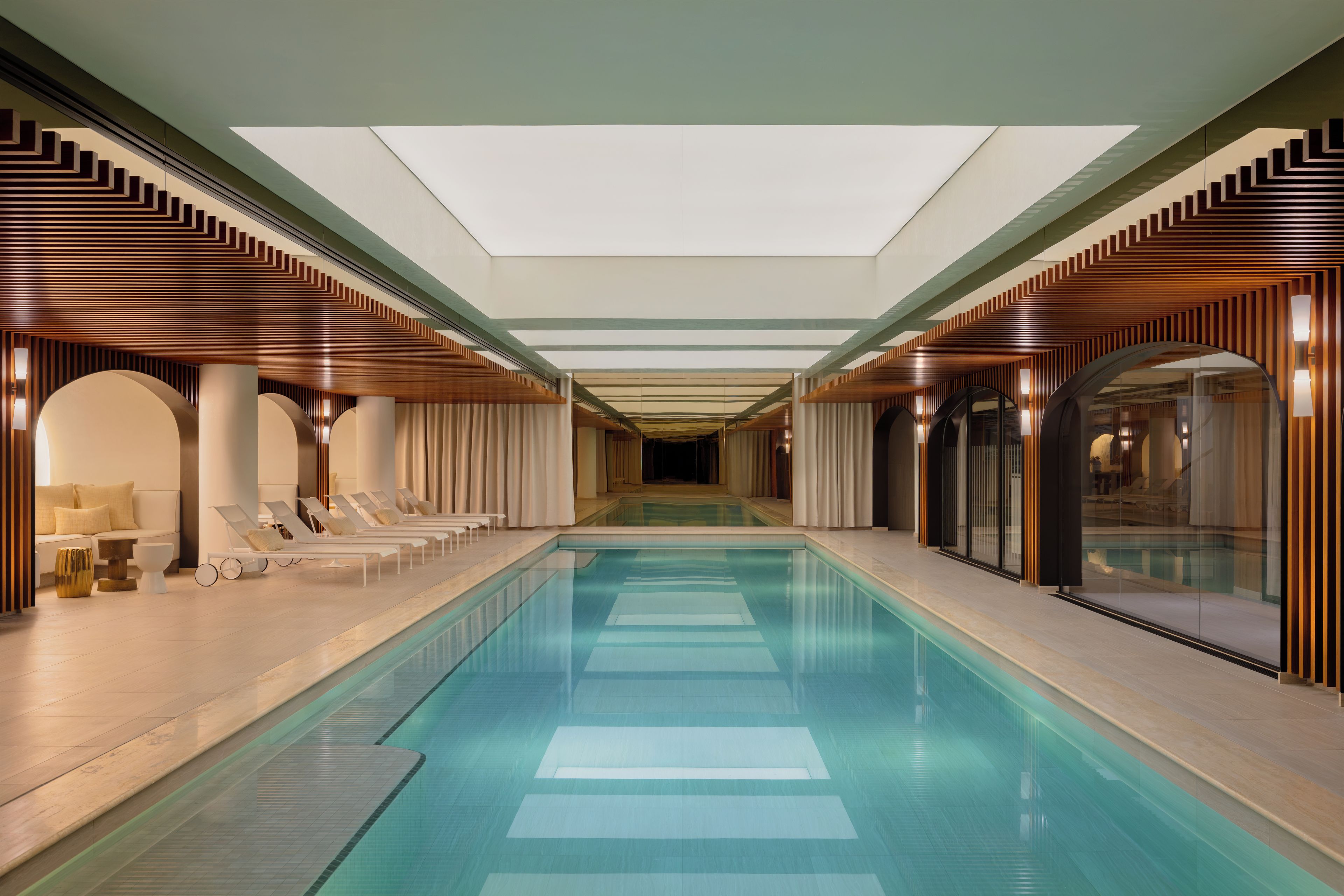 Ein moderner, überdachter Pool mit Liegestühlen und einer Glaswand auf einer Seite.
