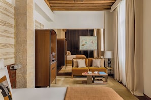 Une chambre d’hôtel moderne avec un plafond en bois, un grand lit, un canapé, une table basse et un tableau au mur.
