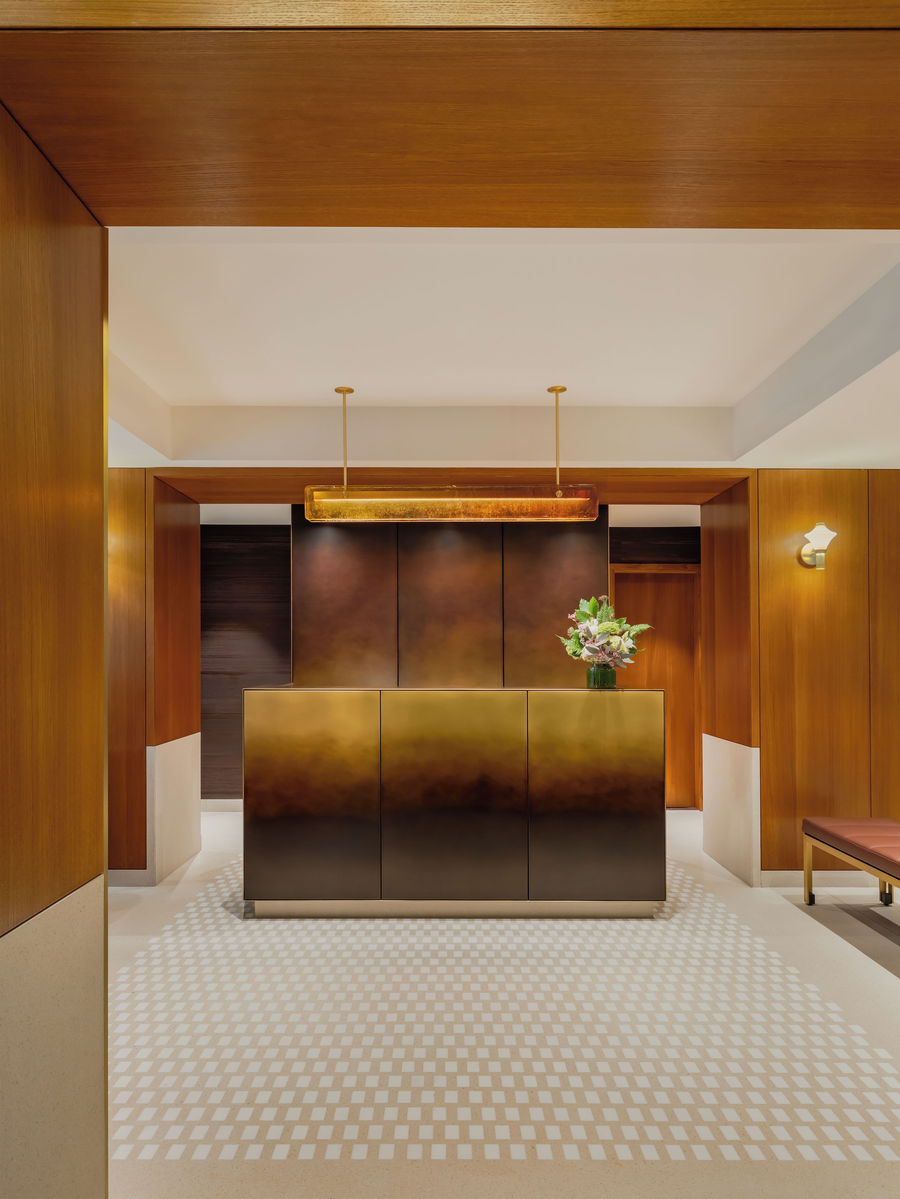A reception area with a modern design, featuring a wooden reception desk, a patterned floor, and a wall-mounted light fixture.