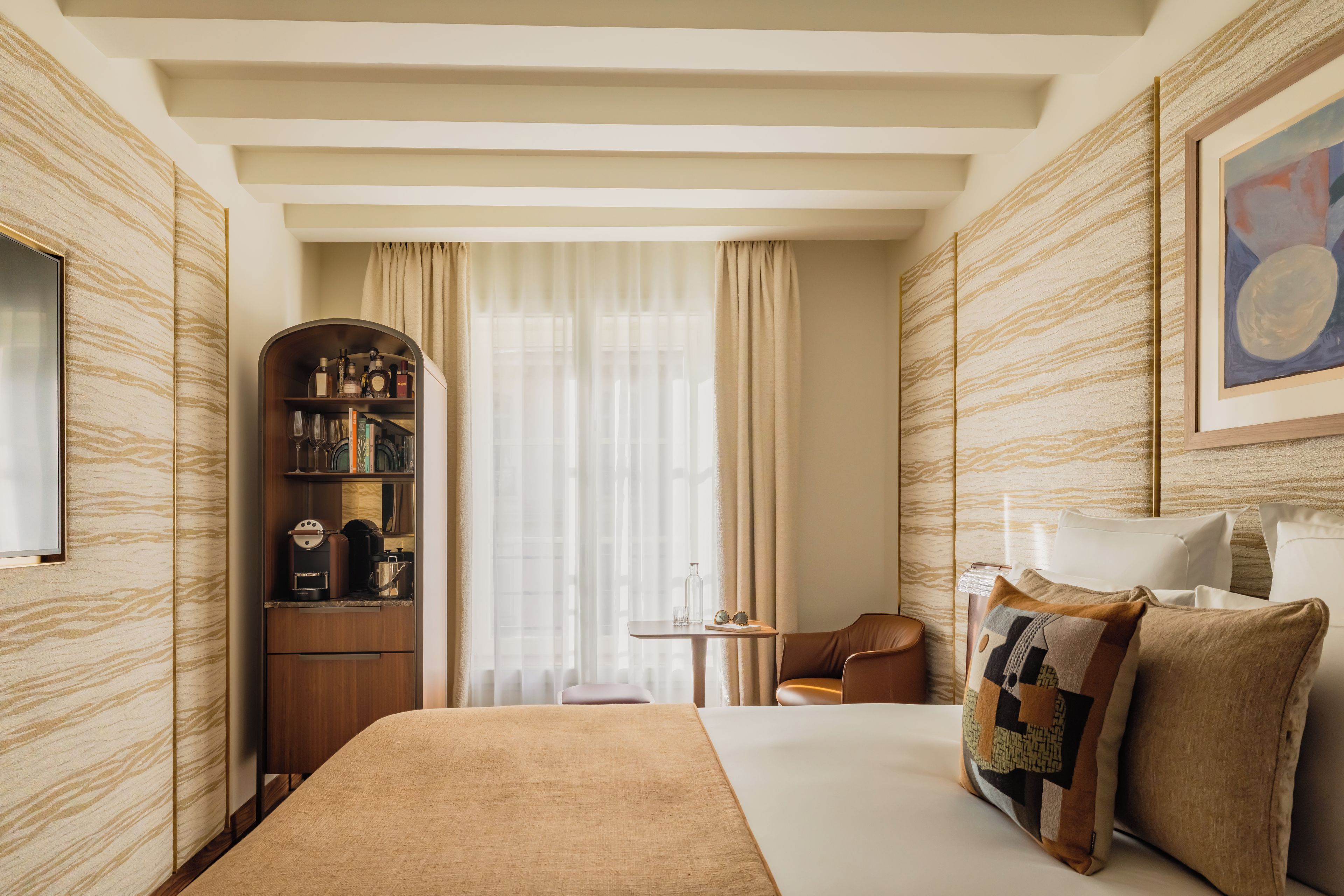 A hotel room with a large bed, a seating area with a table, a bookshelf, and a painting on the wall.