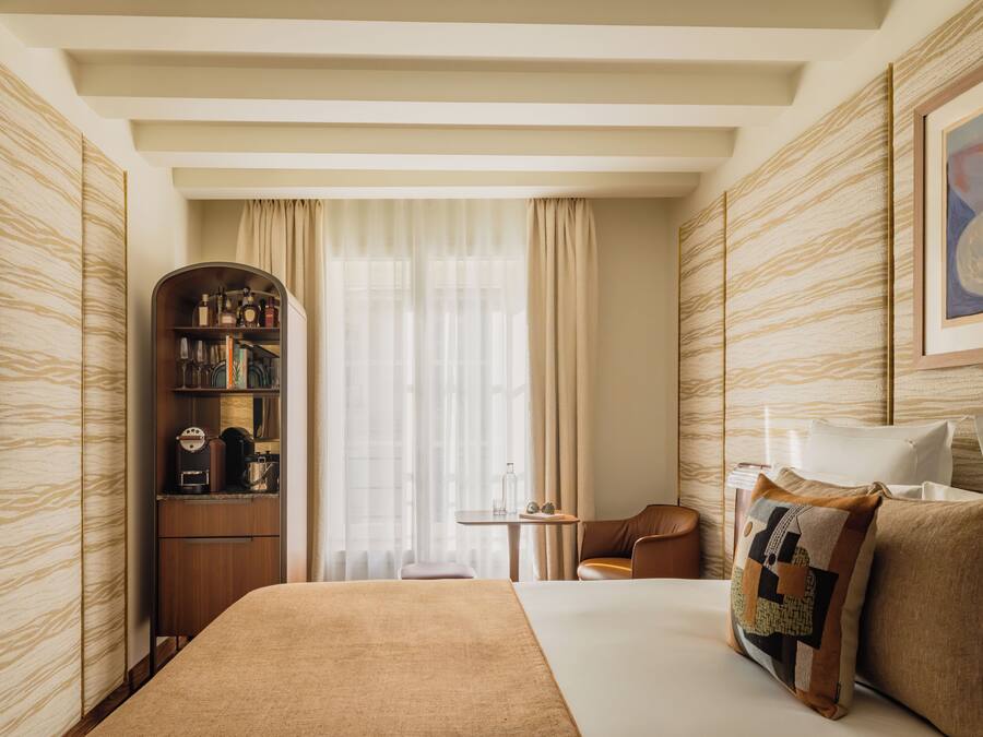 Habitación de hotel con una cama grande, un área de descanso con una mesa, una estantería y un cuadro en la pared.