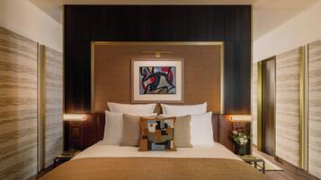 A hotel room with a large bed, a painting above the headboard, and a nightstand with a lamp.