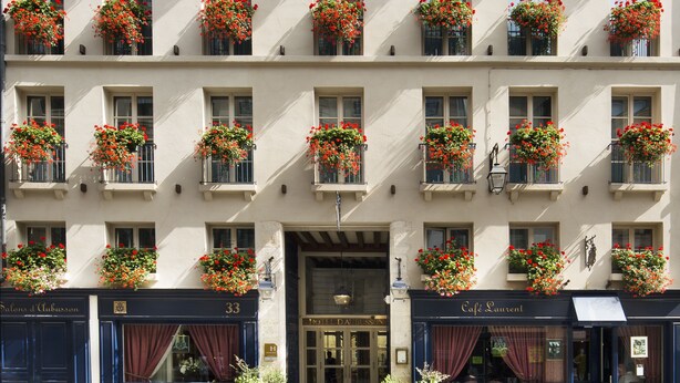 A hotel facade with multiple windows adorned with red flowers, a prominent entrance, and signage for 'Hotel Da Blisson' and 'Café Laurent'.