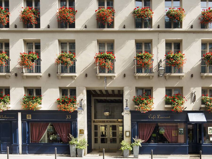 A hotel facade with multiple windows adorned with red flowers, a prominent entrance, and signage for 'Hotel Da Blisson' and 'Café Laurent'.