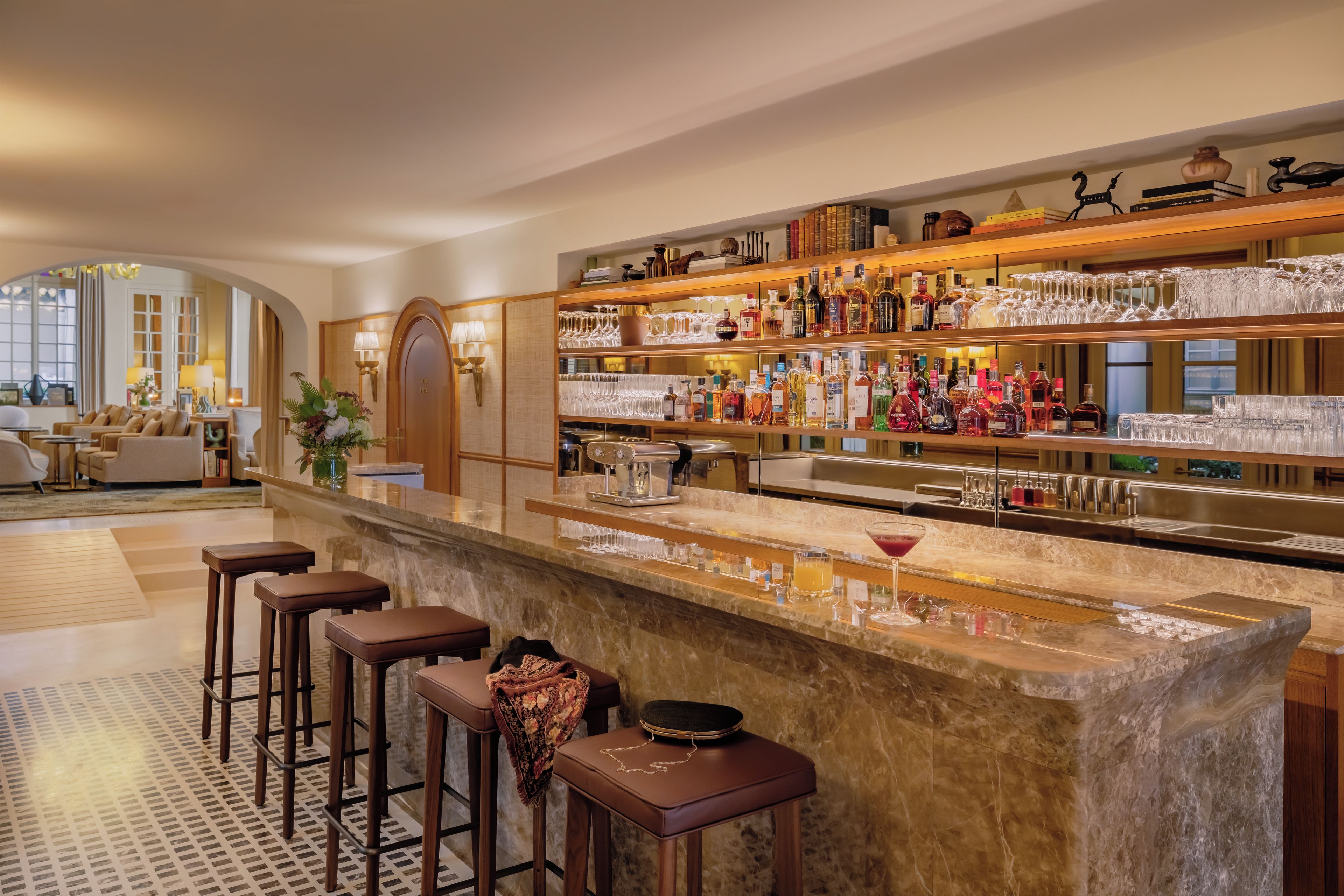 A bar area with a marble countertop, multiple stools, and a variety of bottles and glasses.