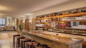 A bar area with a marble countertop, multiple stools, and a variety of bottles and glasses.