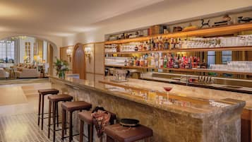 A bar area with a marble countertop, multiple stools, and a variety of bottles and glasses.