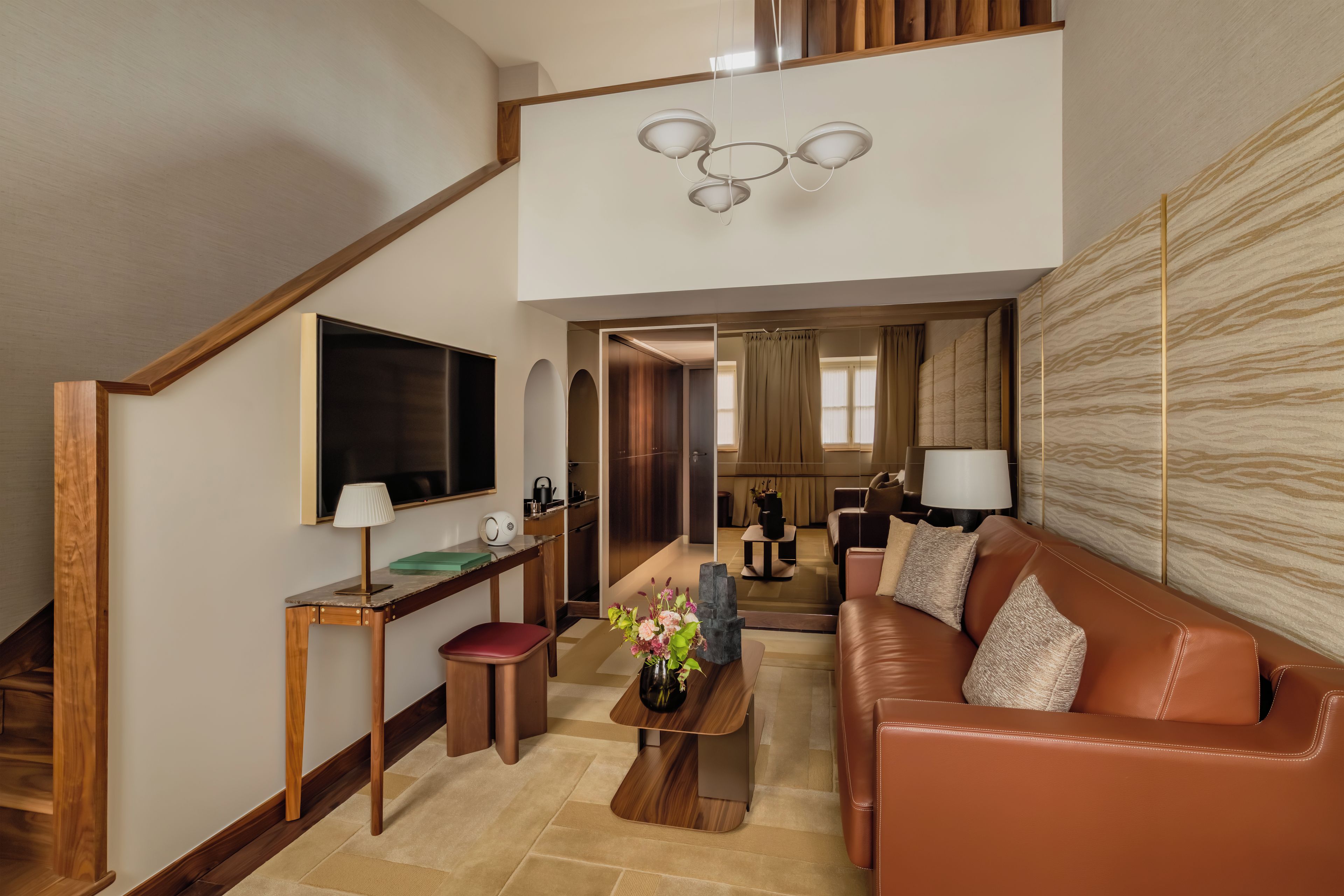 Ein modernes Wohnzimmer mit einem braunen Ledersofa, einem Holztisch, einem an der Wand befestigten Fernseher und einer Treppe zu einer oberen Ebene.