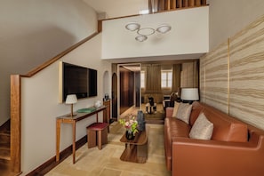 Un salon moderne avec un canapé en cuir marron, une table basse en bois, un téléviseur fixé au mur et un escalier menant à un niveau supérieur.