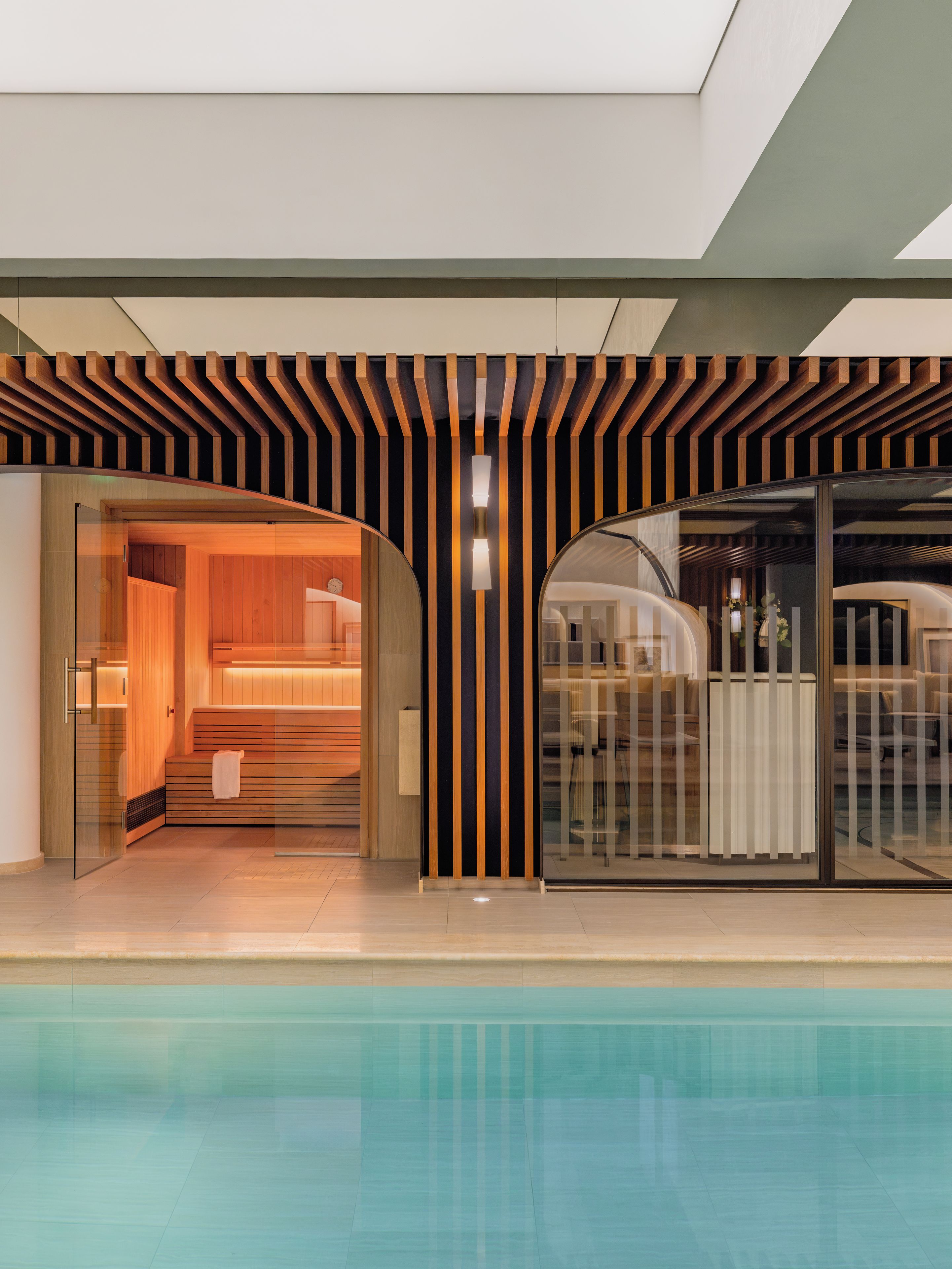 A modern hotel interior with a glass-enclosed pool, a sauna area, and a seating area with a view of the pool.