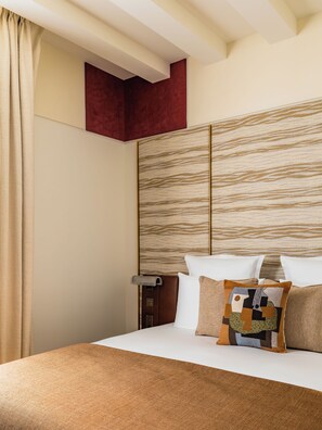 Ein Hotelzimmer mit Bett, Holz-Kopfteil, roter Akzentwand und einem Fenster mit Vorhängen.