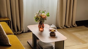 A room with a wooden table, a vase with flowers, and a glass dome with macarons.