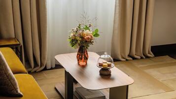 A room with a wooden table, a vase with flowers, and a glass dome with macarons.