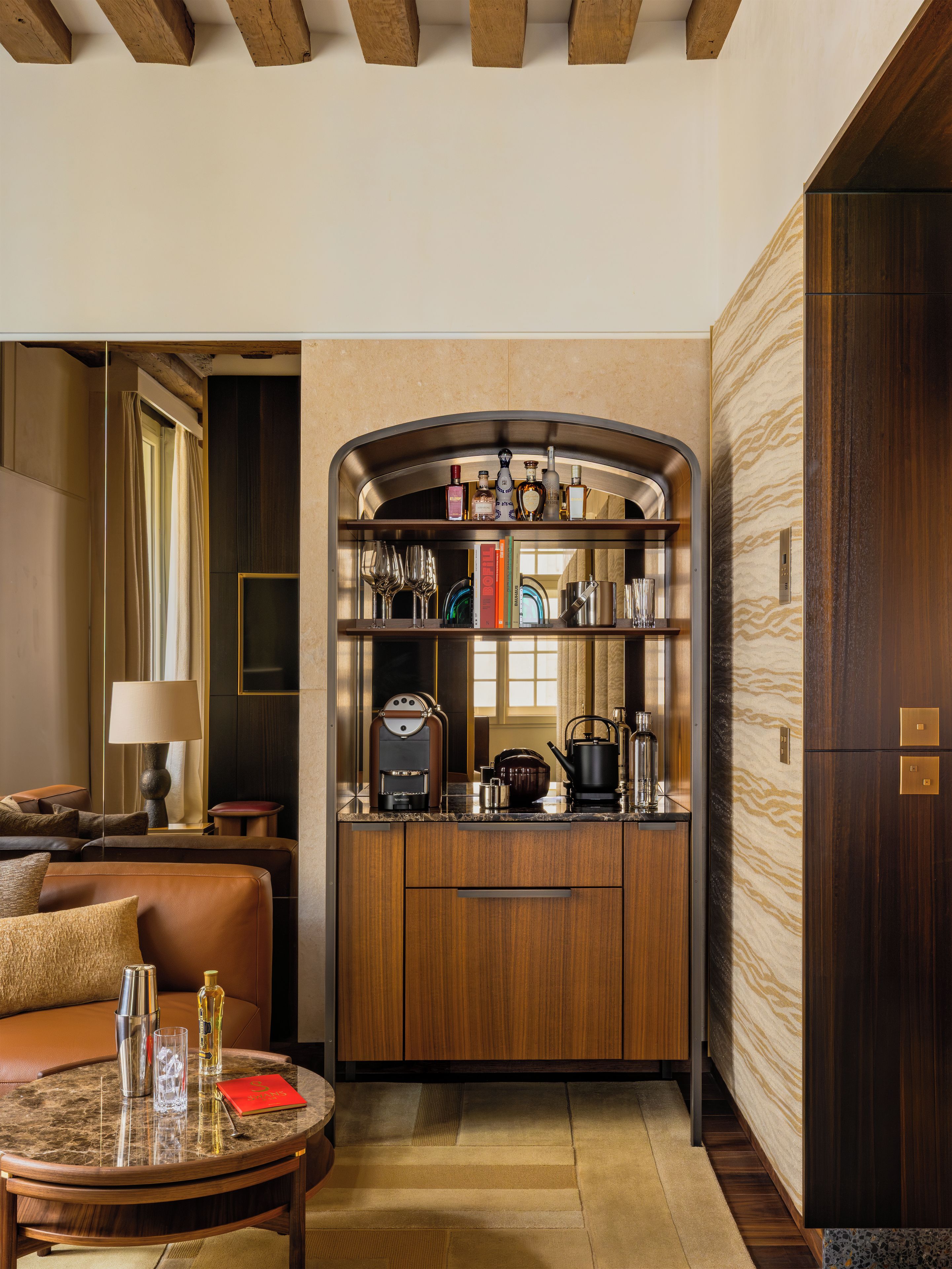 A modern living room with a built-in kitchen area, a seating area with a sofa and a coffee table, and a bookshelf with various items.