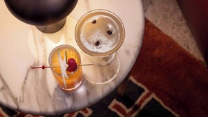 Dois cocktails sobre uma mesa de mármore, com um tapete estampado ao fundo.
