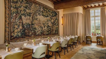 A dining area with tables set for service, a large tapestry on the wall, and a view of the outdoors through a window.