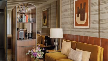 A modern hotel room with a sofa, a coffee table, a bookshelf, and a large abstract painting on the wall.