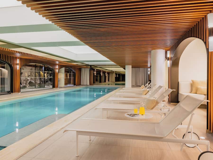 Zona de piscina con sillones de descanso, piscina y techo con diseño de listones de madera.