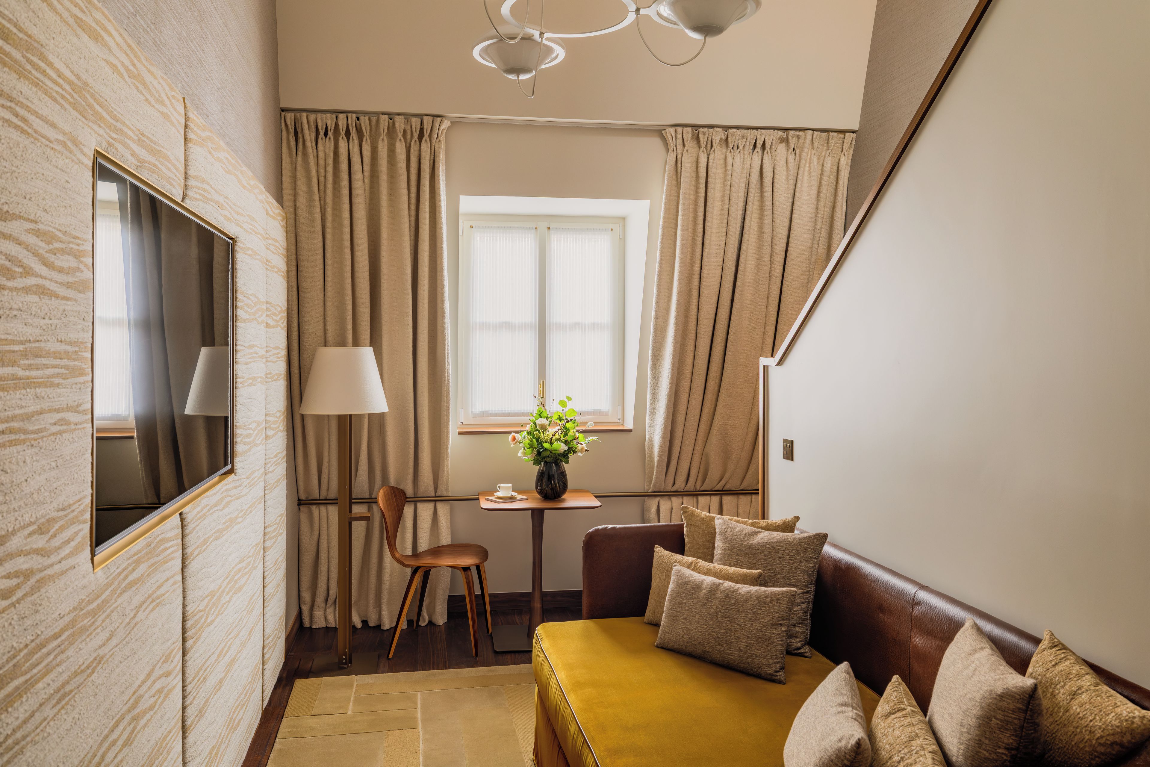 A room with a sofa, a table with a vase of flowers, a chair, and a window with curtains.