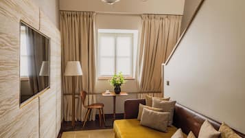 A room with a sofa, a table with a vase of flowers, a chair, and a window with curtains.
