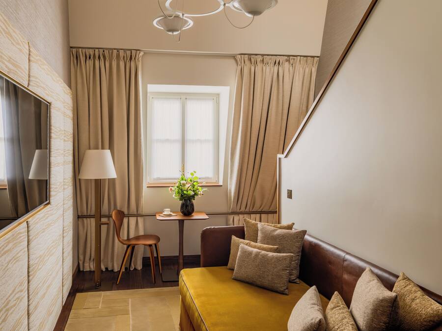 Una habitación con un sofá, una mesa con un jarrón de flores, una silla y una ventana con cortinas.