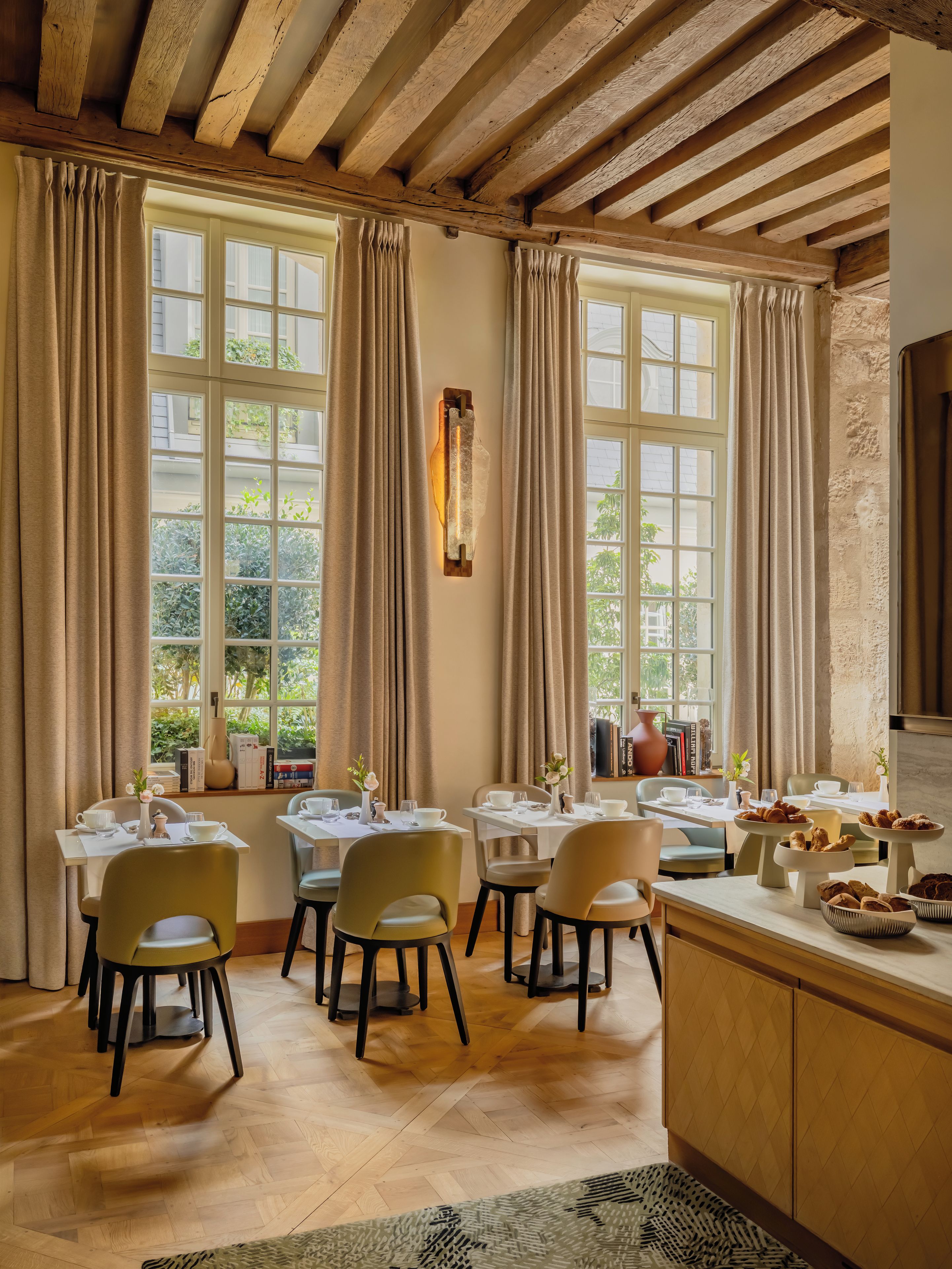Un comedor con vigas de madera, ventanas amplias con cortinas y una mesa de buffet con pastelería.