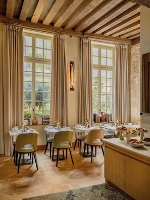 A dining area with wooden beams, large windows with curtains, and a buffet table with pastries. - Hotel d'Aubusson (Paris)
