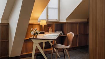 A modern loft bedroom with a sloped ceiling, a wooden desk, a chair, a lamp, and a bookshelf.
