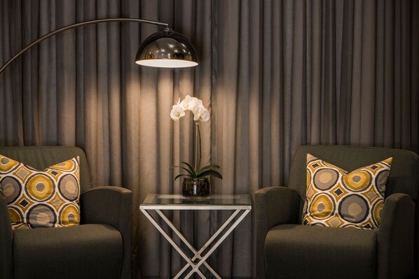 A room with two armchairs, a small table with a vase of flowers, and a floor lamp.